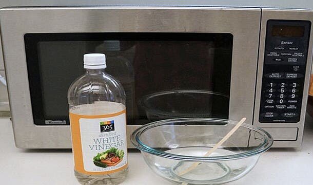 Bouteille de vinaigre à côté d'un bol d'eau, le tout devant micro-onde
